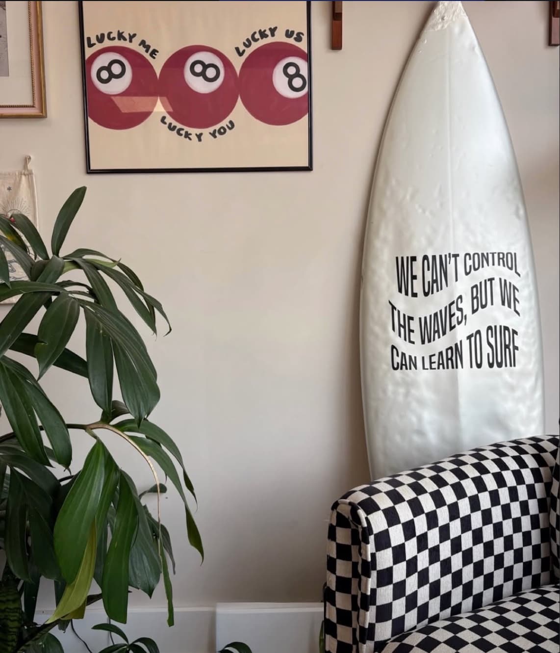A corner of the shop with a surfboard, plants, framed art, and a checkered armchair